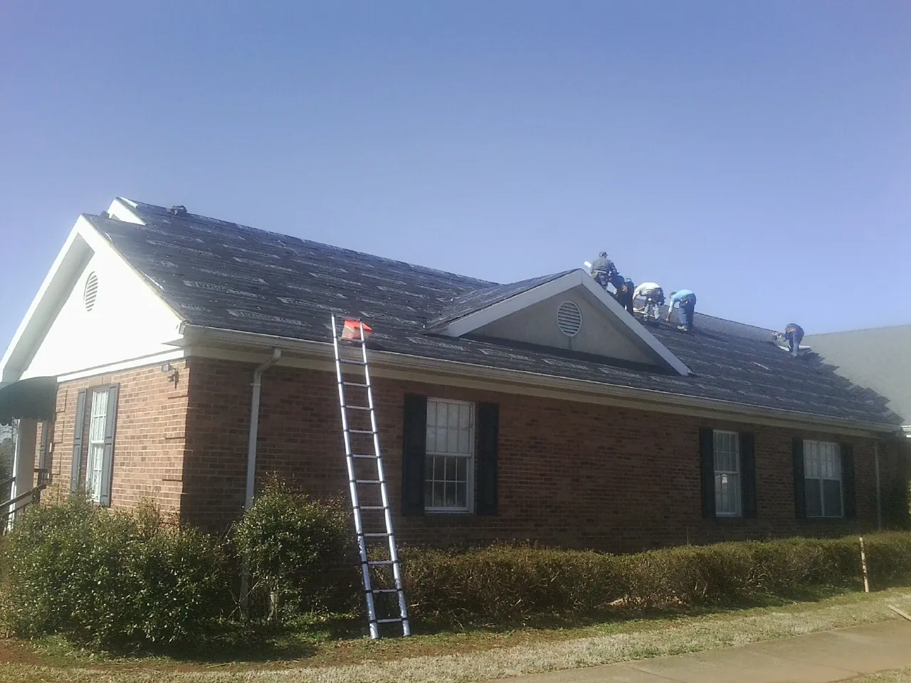Crew tearing shingles off a brick ranch roof with a ladder set — Emergency Roof Repair work by our crew in San Carlos