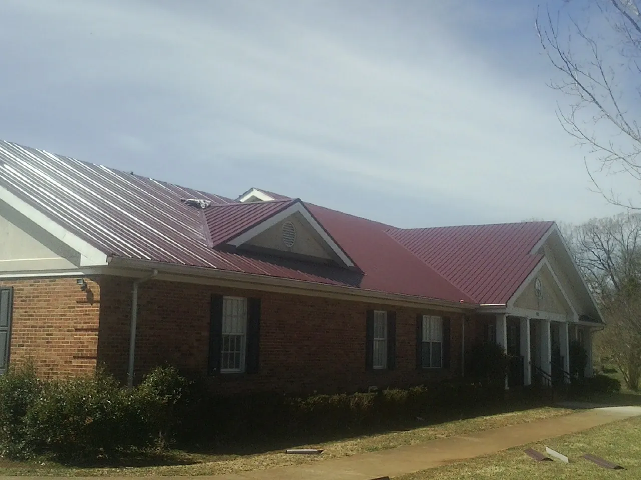Red metal roof with gabled entries on a long brick building, from a Hail Damage Roof Repair job in San Carlos