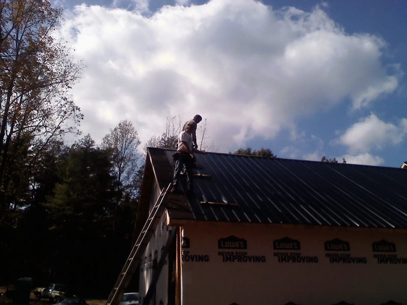Roofer fastening dark metal panels high against a cloudy sky, from a Roof Inspection job in San Carlos
