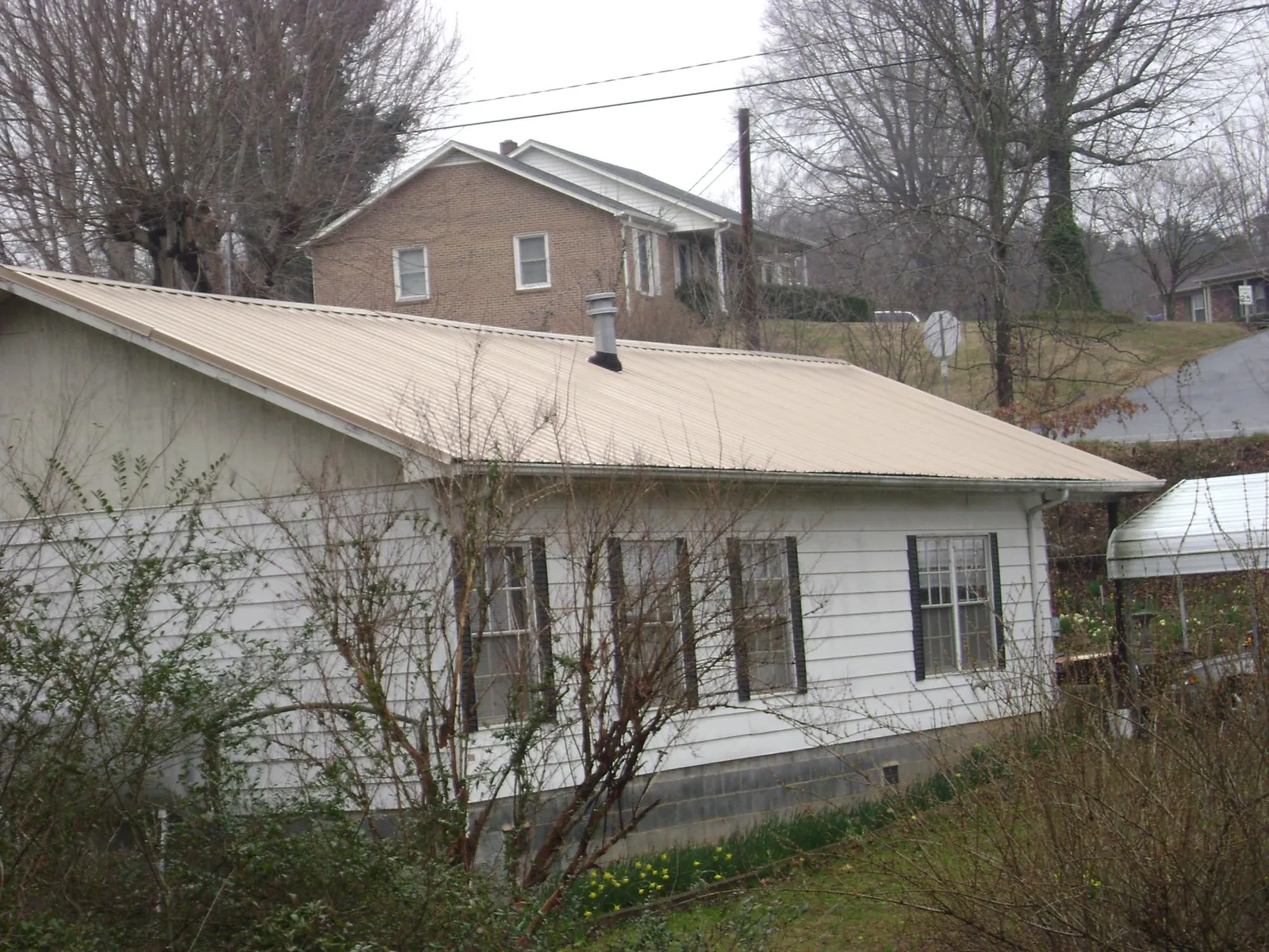 Tan metal roof on a white sided house set into a hillside — Commercial Roofing by Roofing Brothers in San Carlos